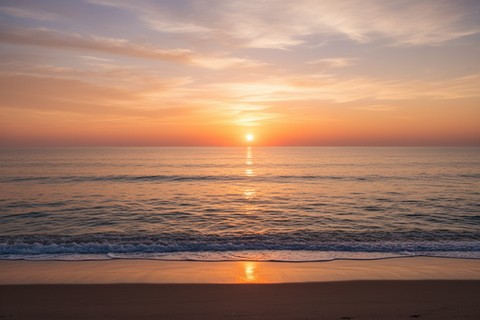 Warm orange light over the ocean horizon, with gentle waves and reflected sunlight on a sandy beach.